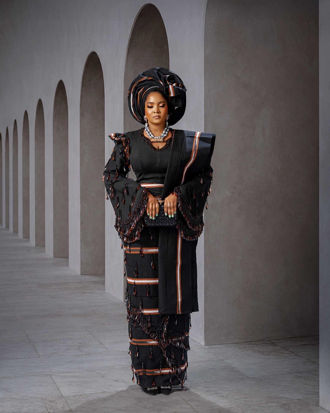 Black occasion outfit with copper-striped detailing and a matching gele