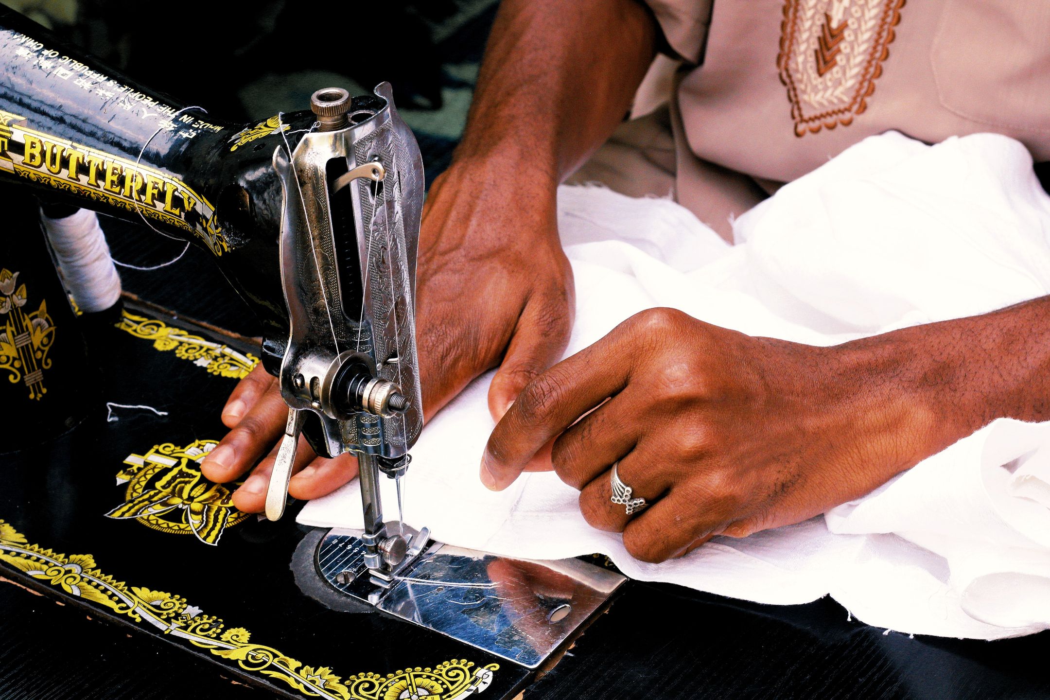 An Abuja tailor guiding white fabric through a sewing machine